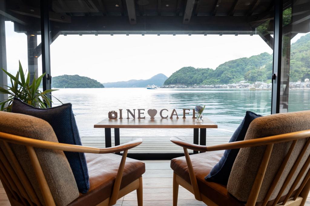 Two chairs on a wooden deck overlooking the bay. A table with wooden letters spell out "Ine Cafe."