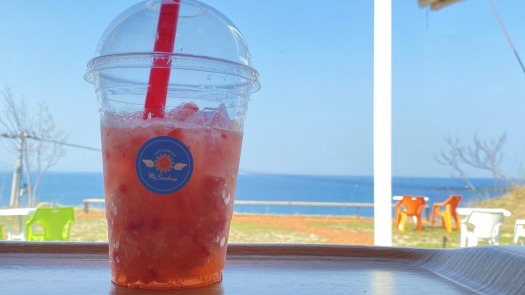 Bright red strawberry fruit tea featured on a table with the ocean in the background