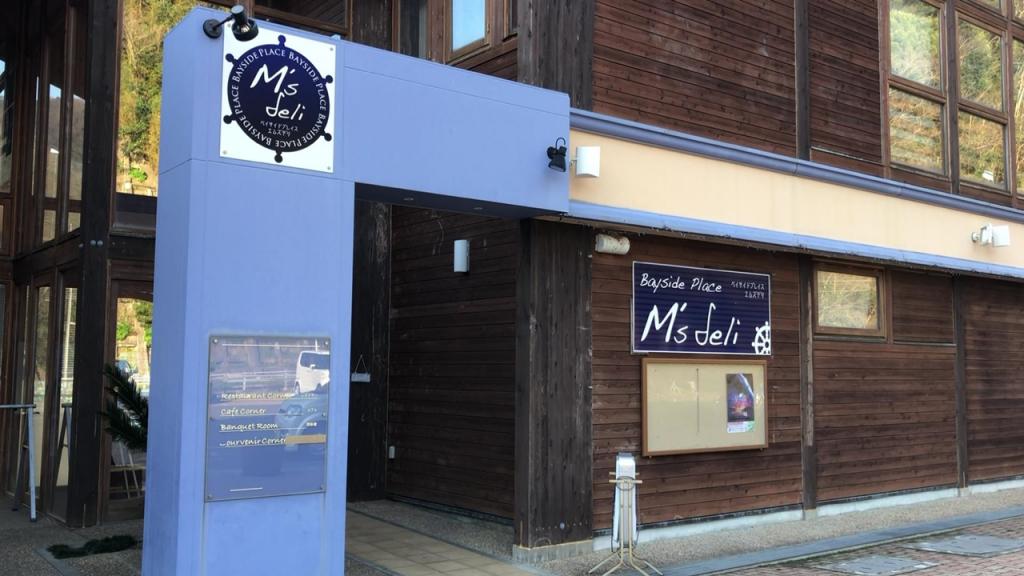 An old wooden building with a big blue sign that says "Bayside Place M's Deli"