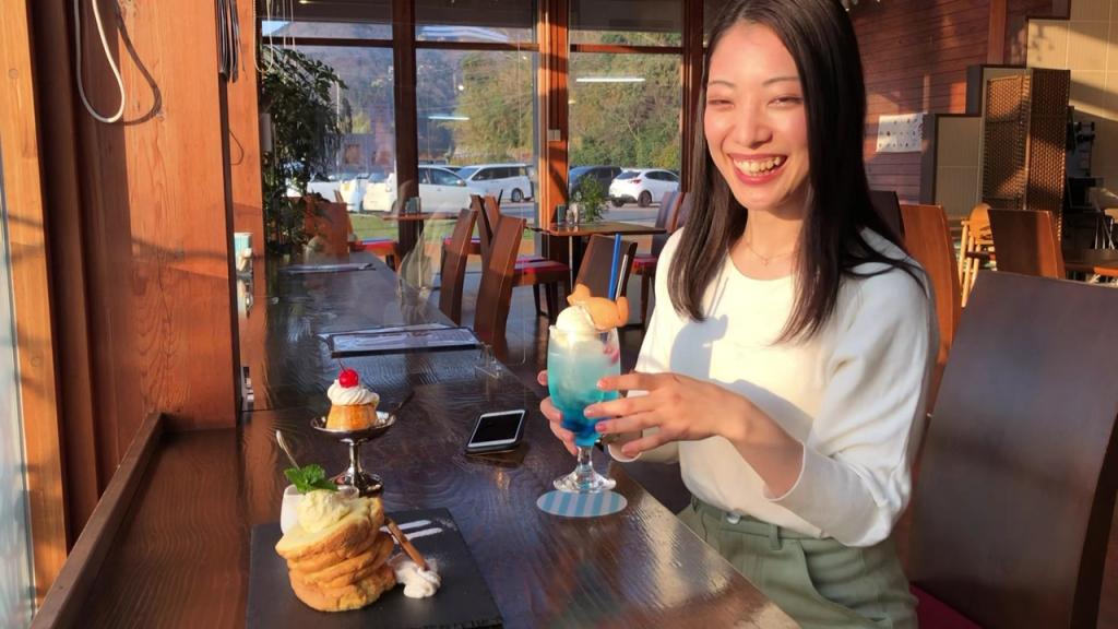 A woman inside a cafe with an assortment of sweets including pancakes, pudding, and an ice cream float.